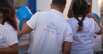 People in white shirts with printed logo of the Sports Paths, gathered together outdoors at an event.